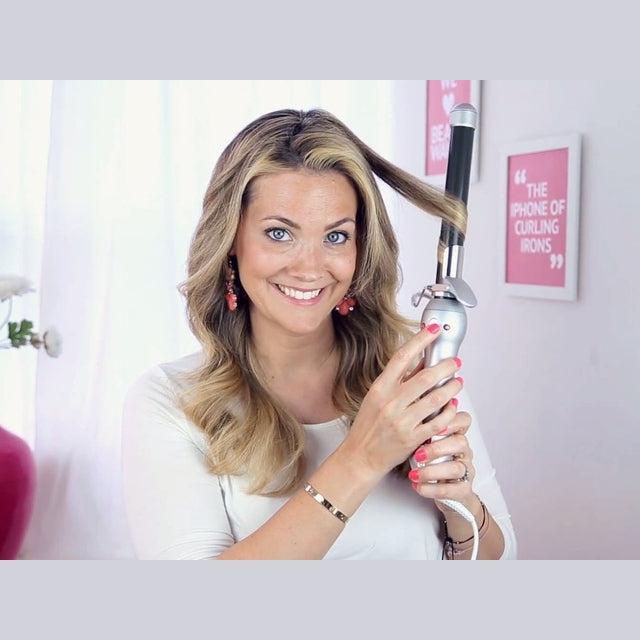 Woman styling her hair with the Beachwaver PRO 1 curling iron, holding a section wrapped around the barrel