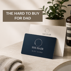 A navy blue and white SSS Hair gift card is displayed in a styled setting with a potted plant and a bottle in the background, with text overlay reading 'THE HARD TO BUY FOR DAD'.