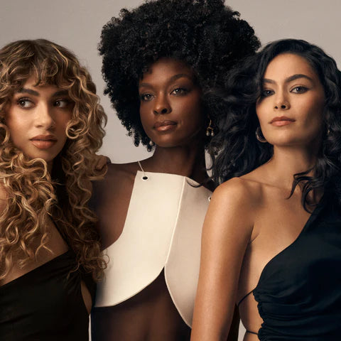 Three women with diverse hairstyles and outfits standing together against a neutral background showing results of Oribe Eternal Curls Moisturizing Shampoo 