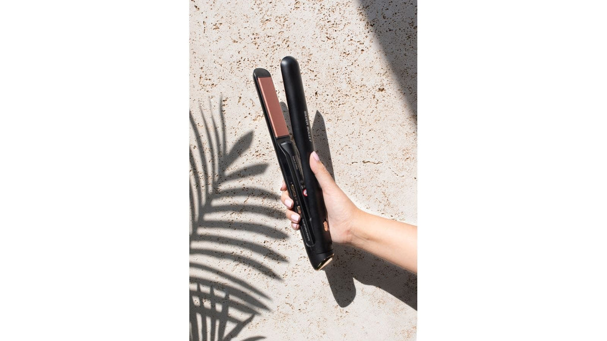 Hand holding Silver Bullet cordless hair straightener outdoors against textured wall