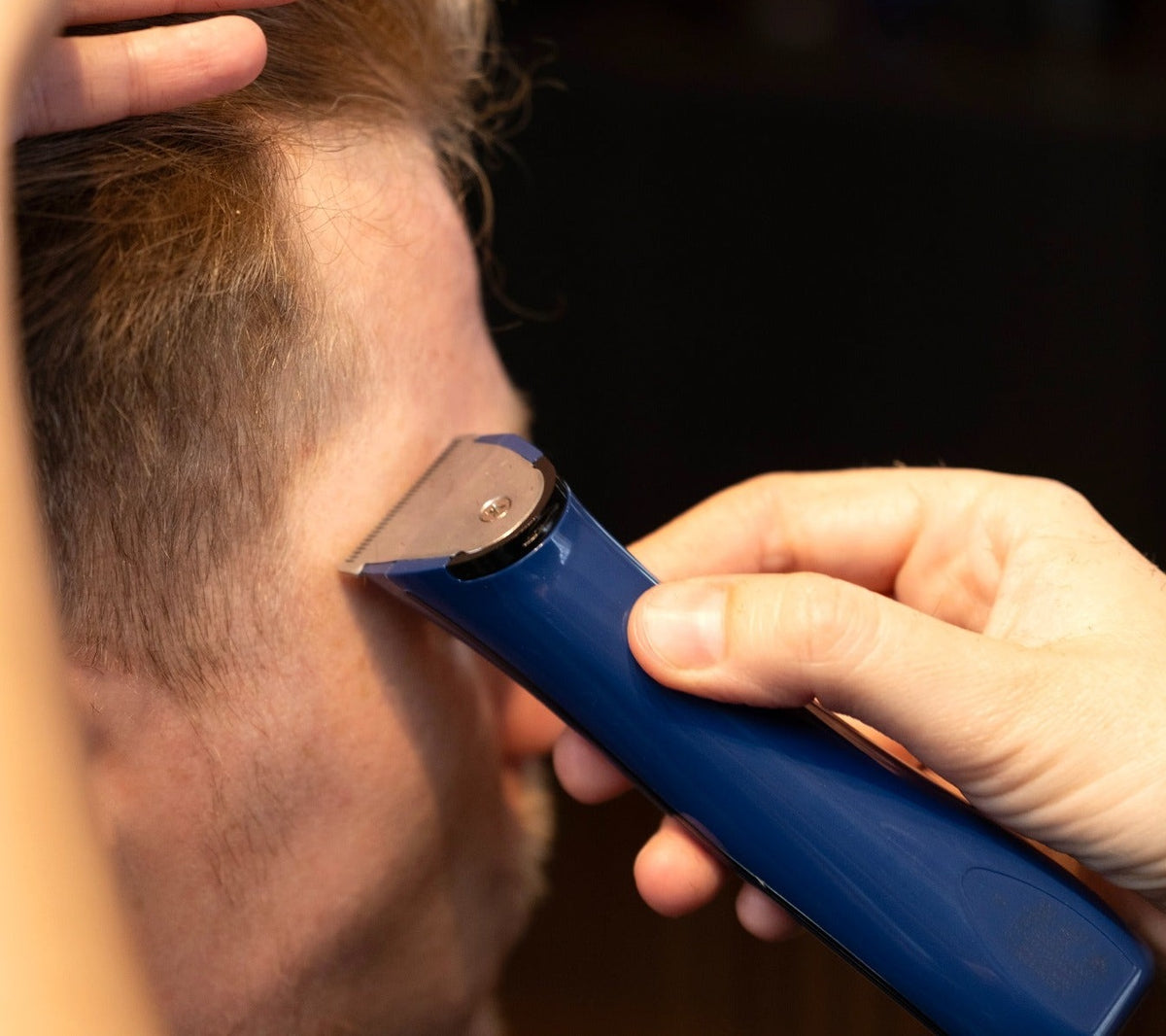 Close-up of blue Wahl Beret trimmer detailing hairline around client’s temple